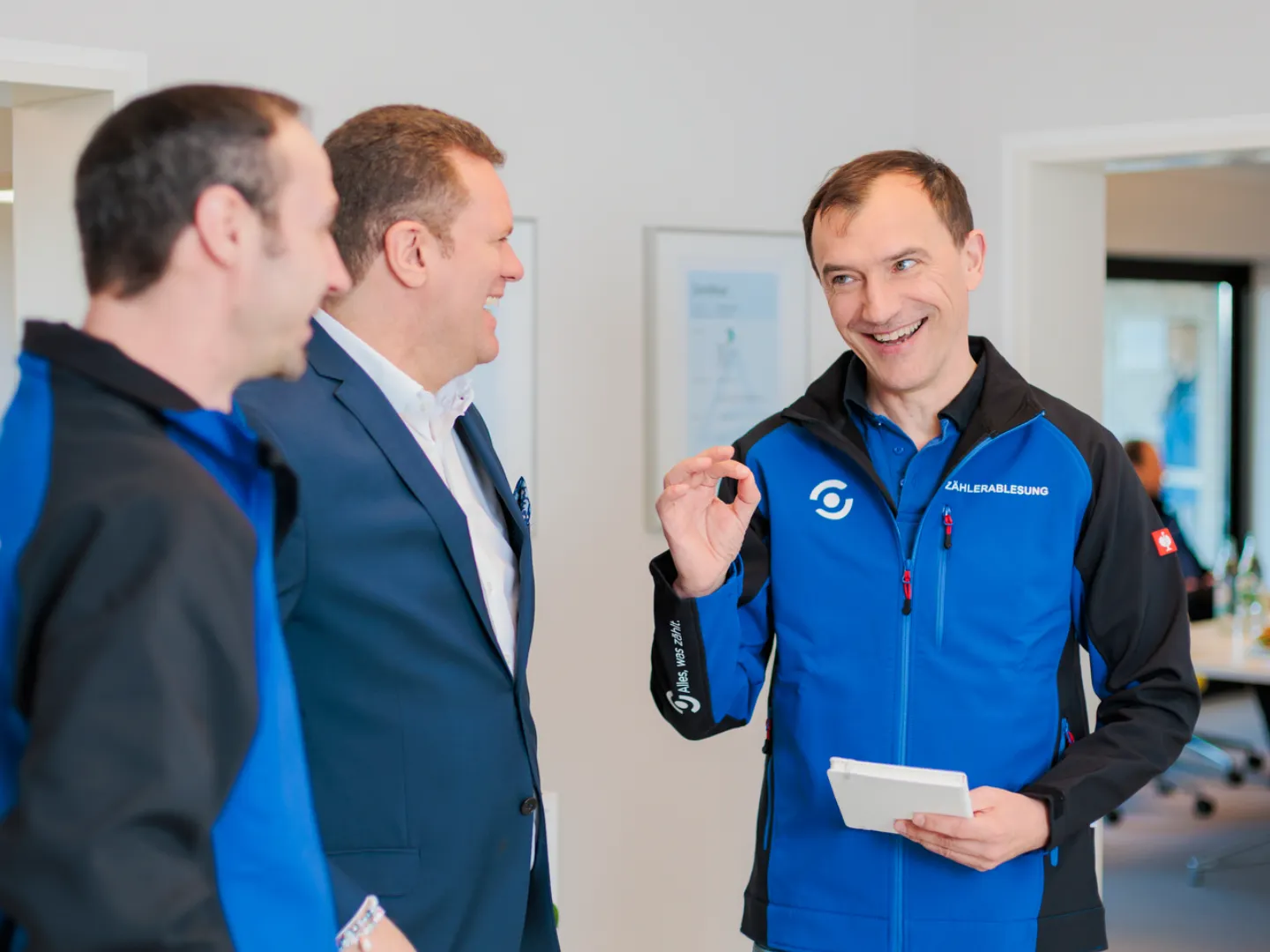 Andrea Schmitt im Büro von Schmitt Zählerstand Gmbh im Gespräch mit zwei Mitarbeitern. Alle lachen fröhlich.